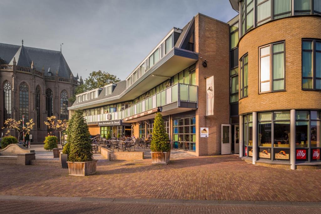 un groupe de bâtiments avec des arbres et une église dans l'établissement Hotel Restaurant De Zwaan, à Raalte