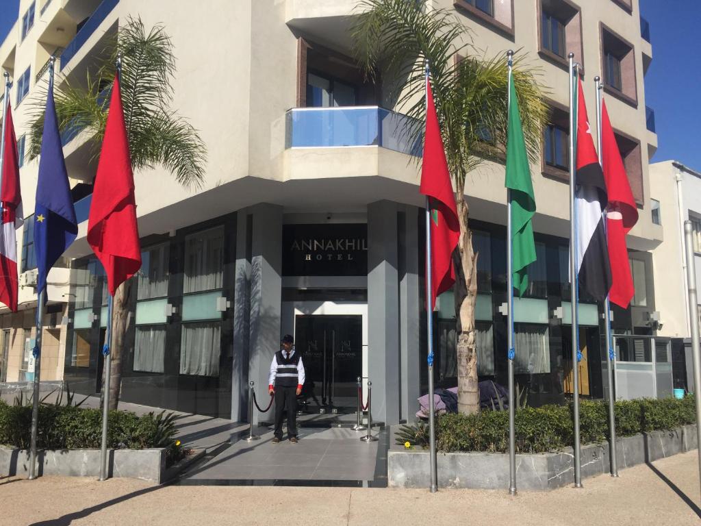 Un uomo in piedi di fronte a un edificio con delle bandiere di Annakhil Hotel a Rabat