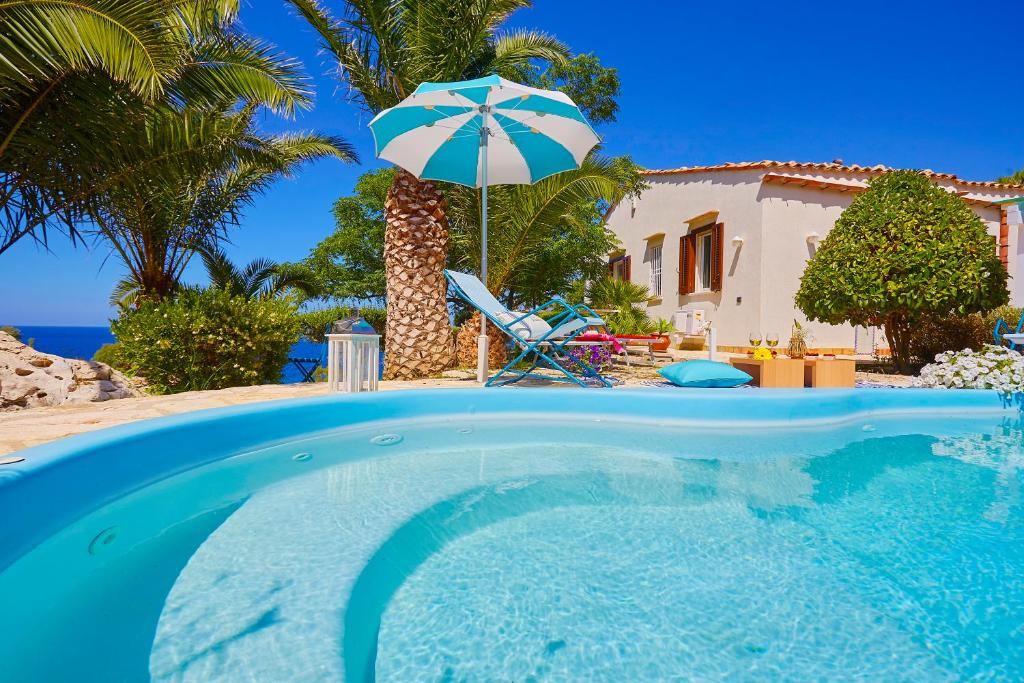 a swimming pool with an umbrella and a house at Villa Ginestra - Scopello-Villas in Scopello