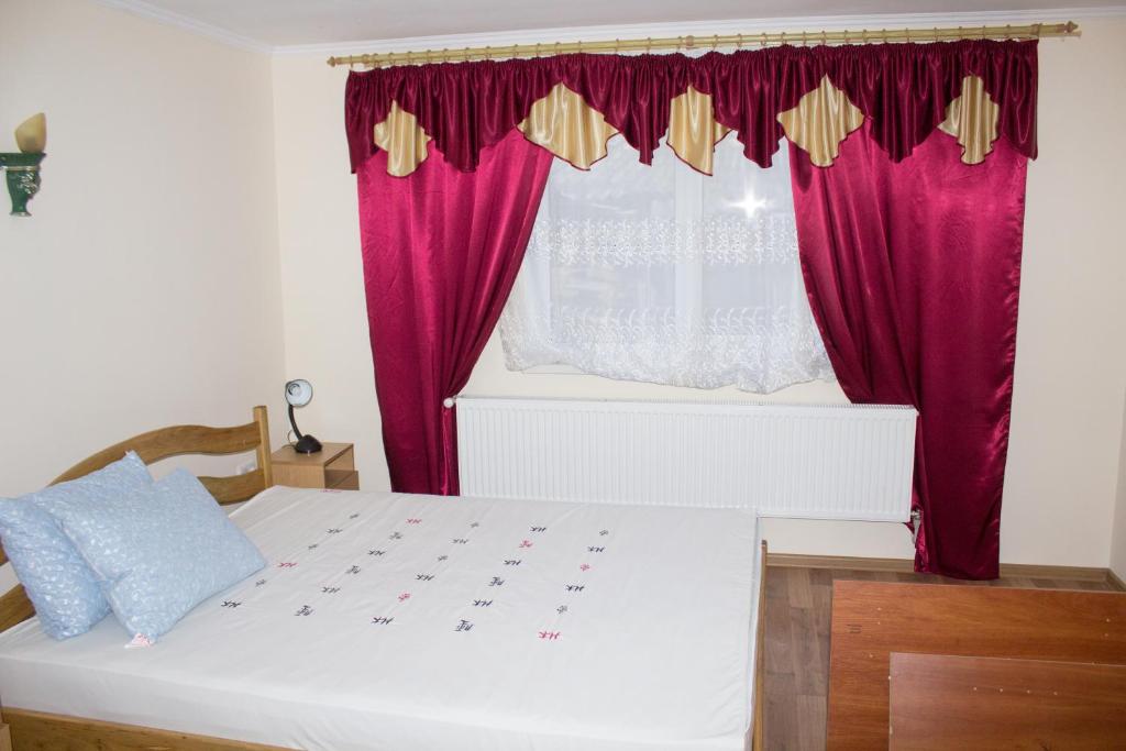 1 dormitorio con cama blanca y cortinas rojas en Імобільяре en Khorostkiv
