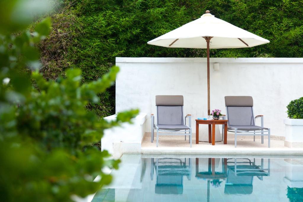 two chairs and a table with an umbrella next to a pool at The Racha in Ko Racha Yai 