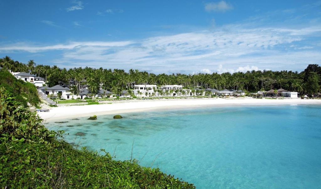 a beach with white sand and blue water and houses at The Racha in Ko Racha Yai 