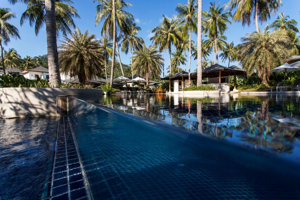 a swimming pool in front of a resort with palm trees at The Racha in Ko Racha Yai 