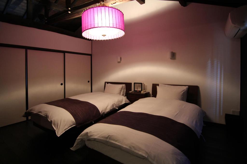 2 Betten in einem Zimmer mit rosa Licht in der Unterkunft Shikoku an Machiya House in Kyoto