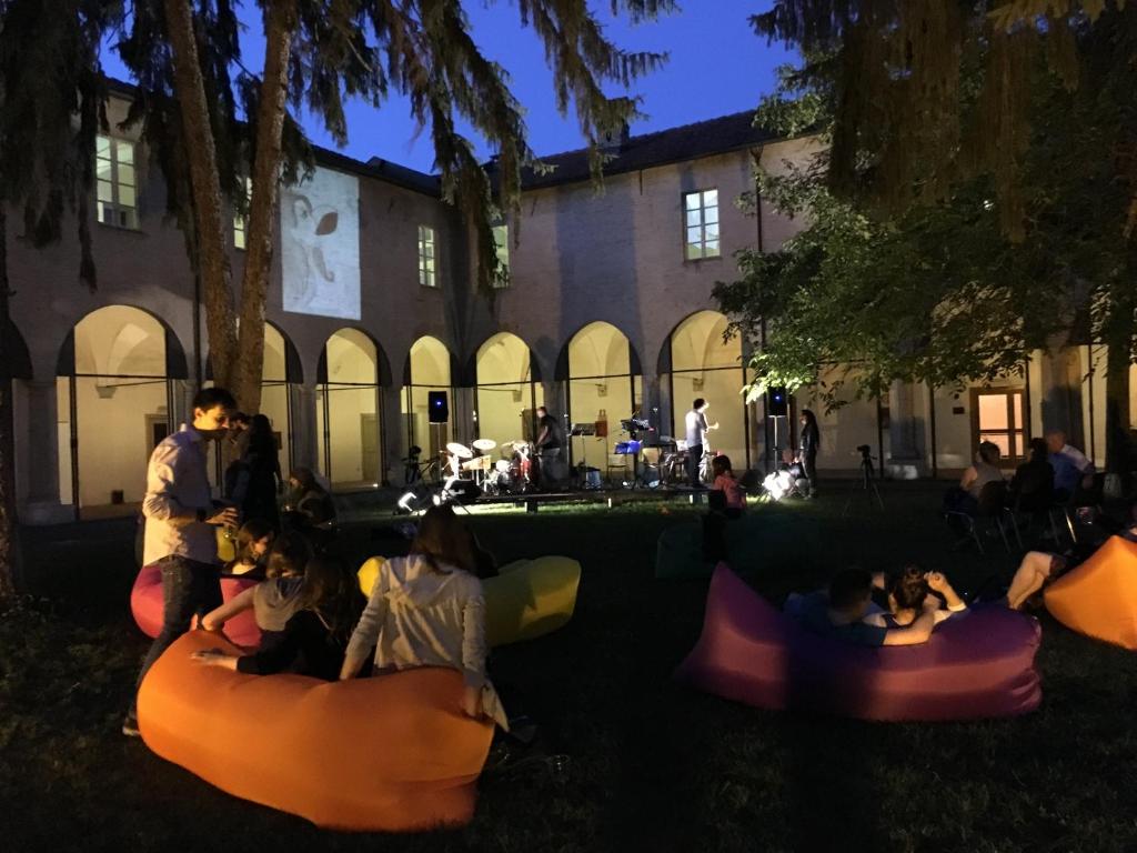 Pessoas sentadas em sacos de feijão na relva em frente a um edifício em Il Chiostro Hostel and Hotel em Alessandria