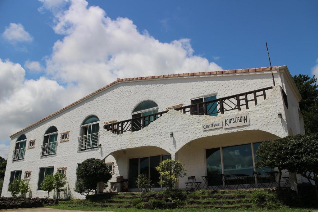 a white building with a balcony on the side of it at Guesthouse Kim's Cabin in Seogwipo