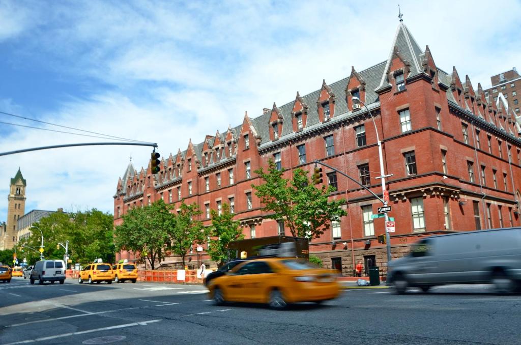 een gele taxi die langs een groot rood bakstenen gebouw rijdt bij HI New York City Hostel in New York