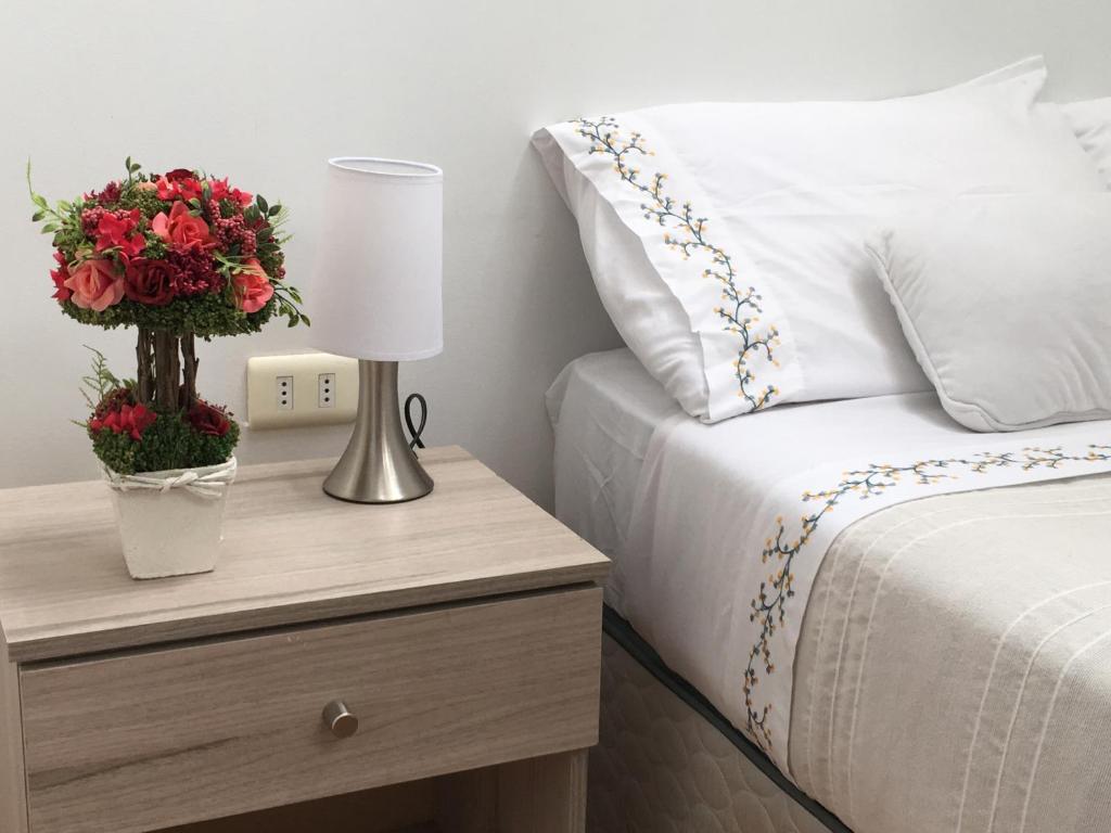 a bed with a table with a lamp and flowers on it at Fragga Hospedaje Boutique in Antofagasta
