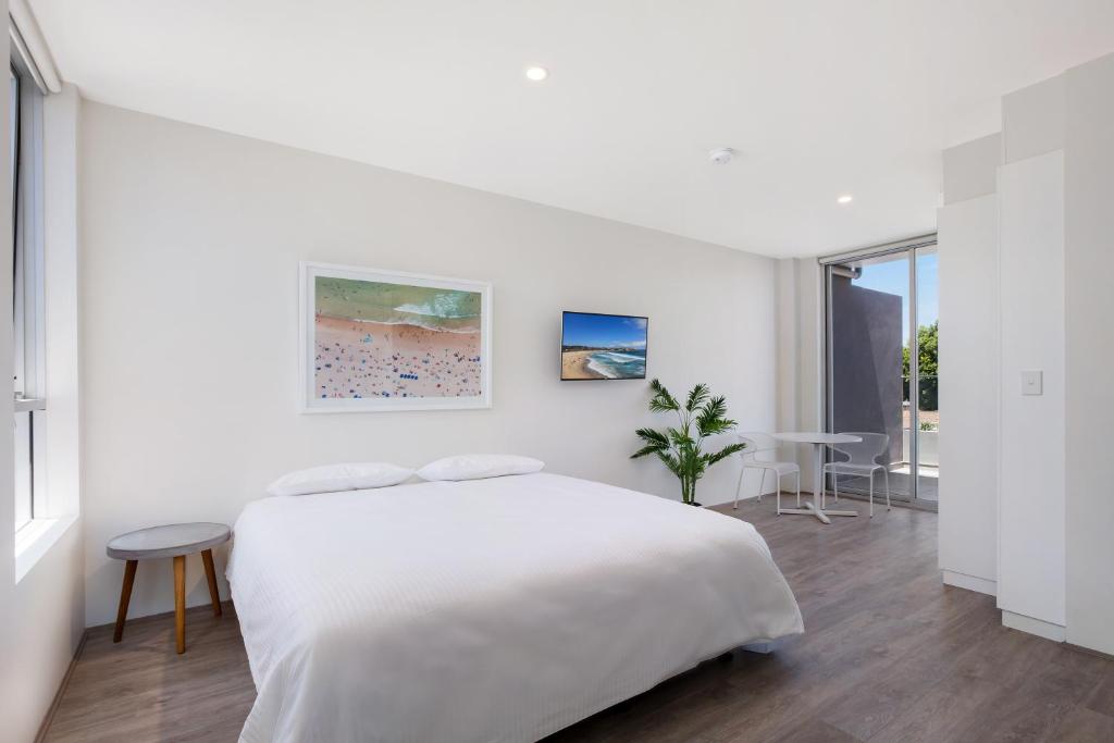 a white bedroom with a large bed and a table at Bondi Beach Studio Penthouse Suite + Balcony in Sydney