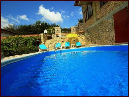 a large blue swimming pool with two chairs and an umbrella at Casa de Artes Guest House in Balchik