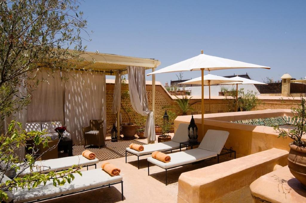 une terrasse avec des canapés, un parasol et une piscine dans l'établissement Riad Tzarra, à Marrakech