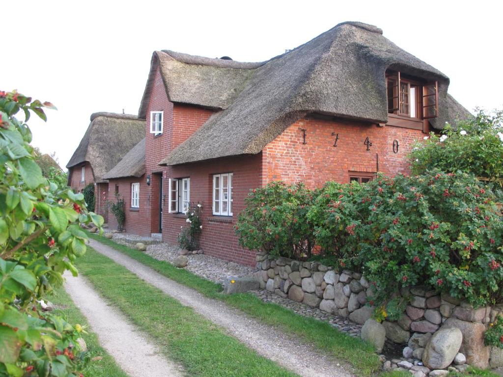 a red brick house with a thatched roof and a stone wall at Haus-an-de-Marsch in Midlum