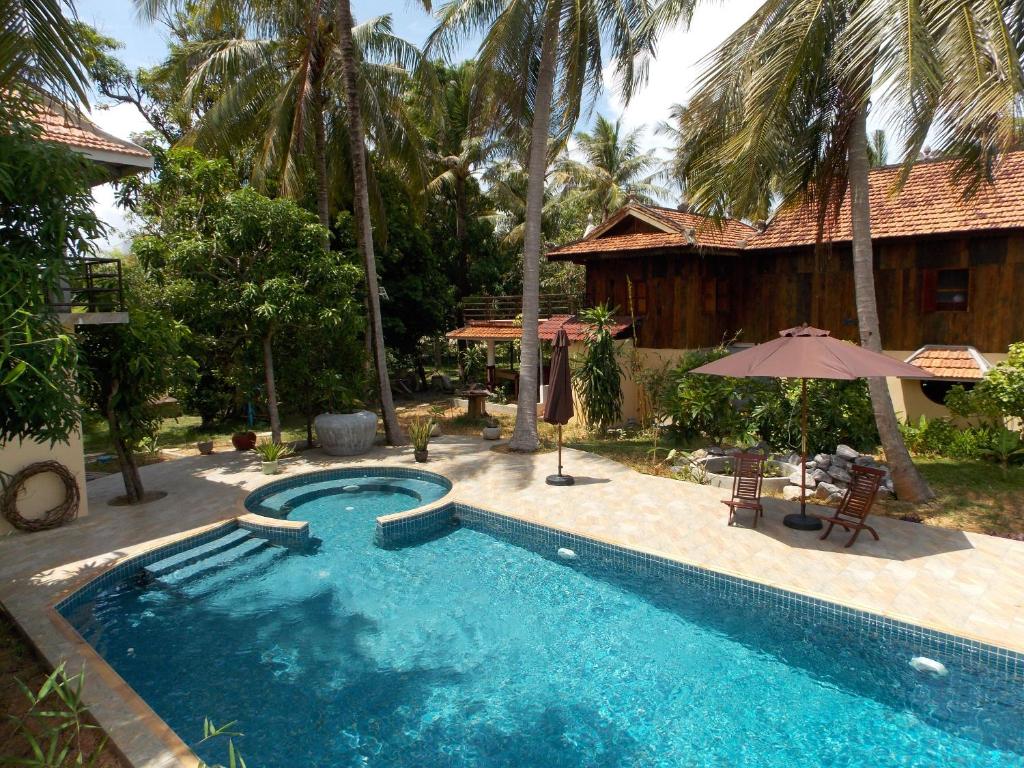 a swimming pool with an umbrella and a house at Le Logis de Kep in Kep