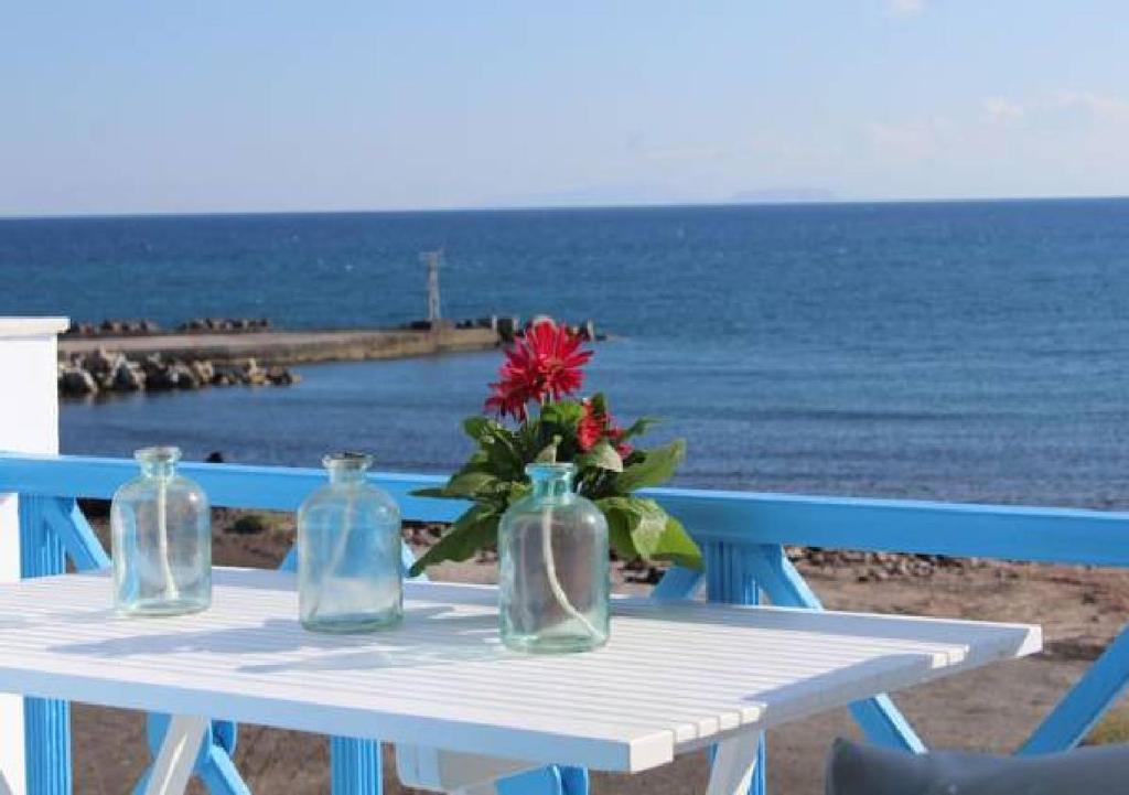 un tavolo bianco con due bottiglie di vetro e un fiore sopra di GeoMare Beach House a Monolithos