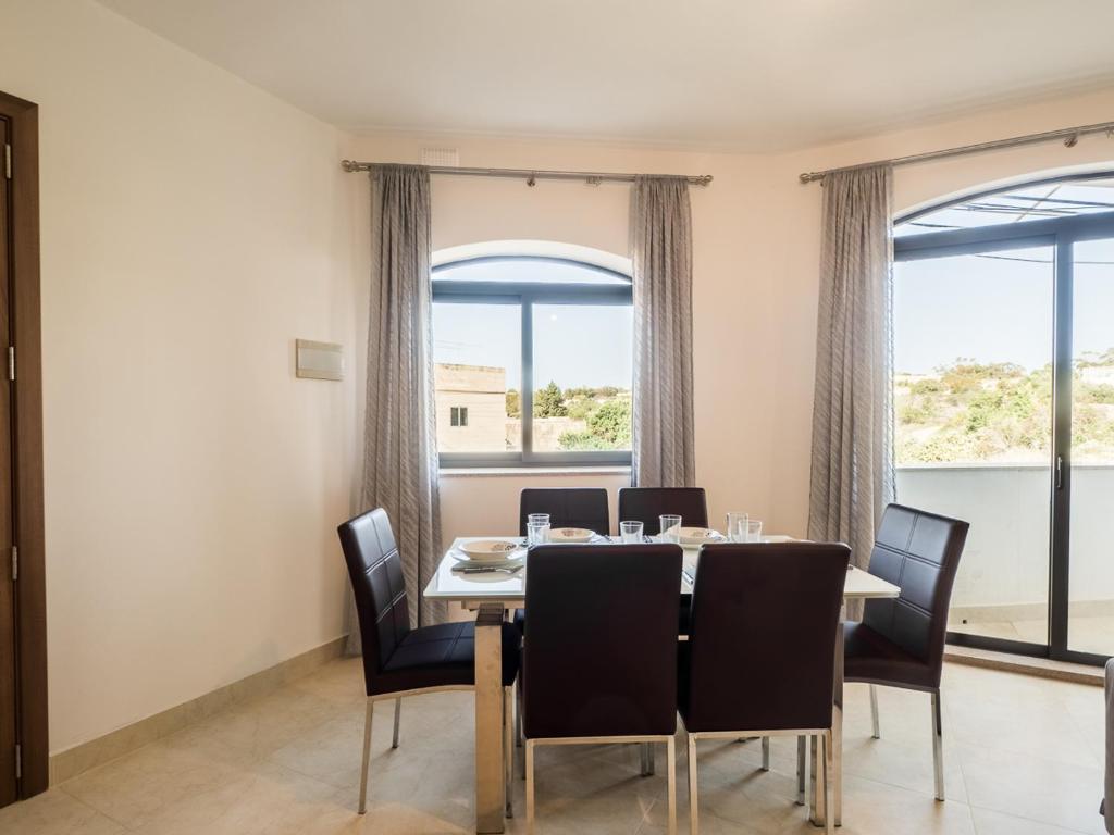 una sala da pranzo con tavolo, sedie e finestre di Landmark Apartment a Birżebbuġa