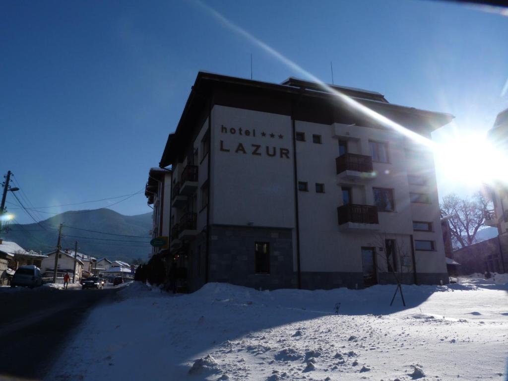 budynek w śniegu ze słońcem za nim w obiekcie Family Hotel Lazur w mieście Bansko