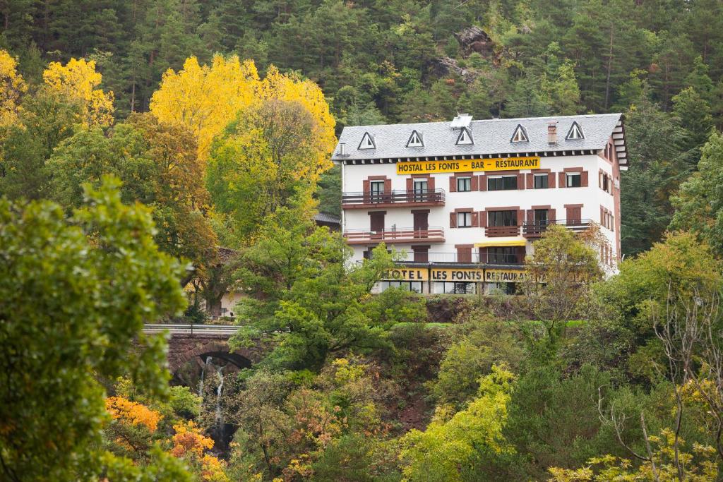 a building on a hill with trees and a bridge at Hostal Les Fonts in Castellar de NʼHug