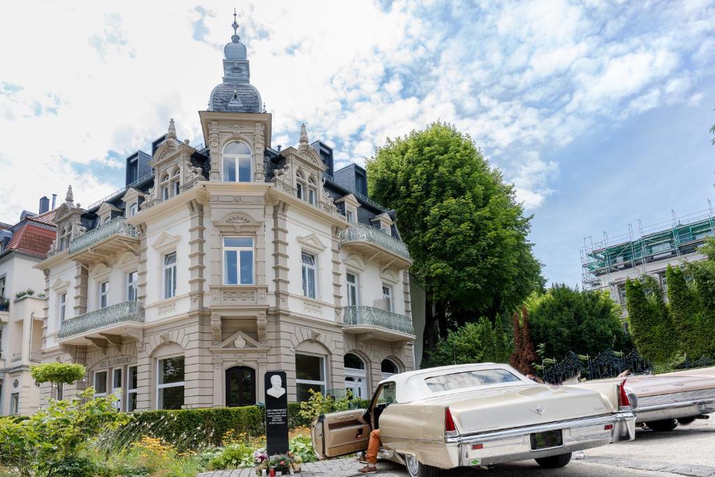 um carro branco estacionado em frente a um edifício com uma torre de relógio em Hotel Villa Grunewald em Bad Nauheim