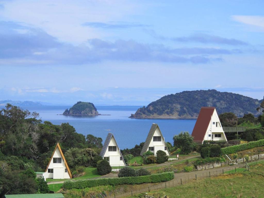 a group of houses on a hill next to the ocean at Pohutukawa Coastal Chalets in Coromandel Town