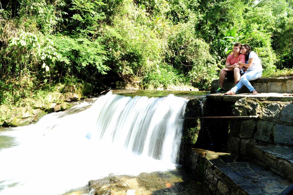 duas pessoas sentadas numa parede perto de uma cascata em Hotel da Cachoeira em Penedo