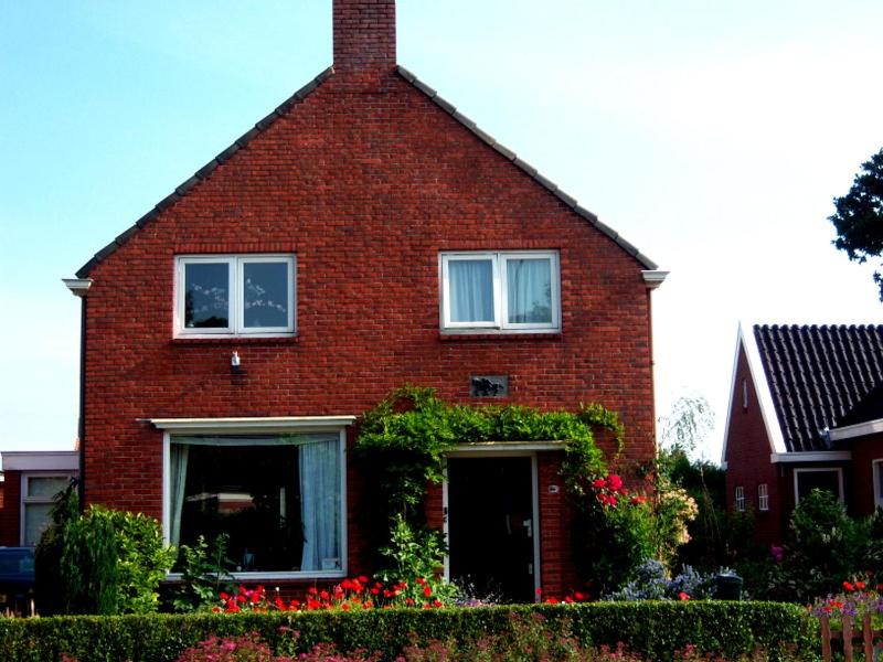de Twee Paardjes في Warffum: منزل من الطوب الأحمر مع الزهور أمامه