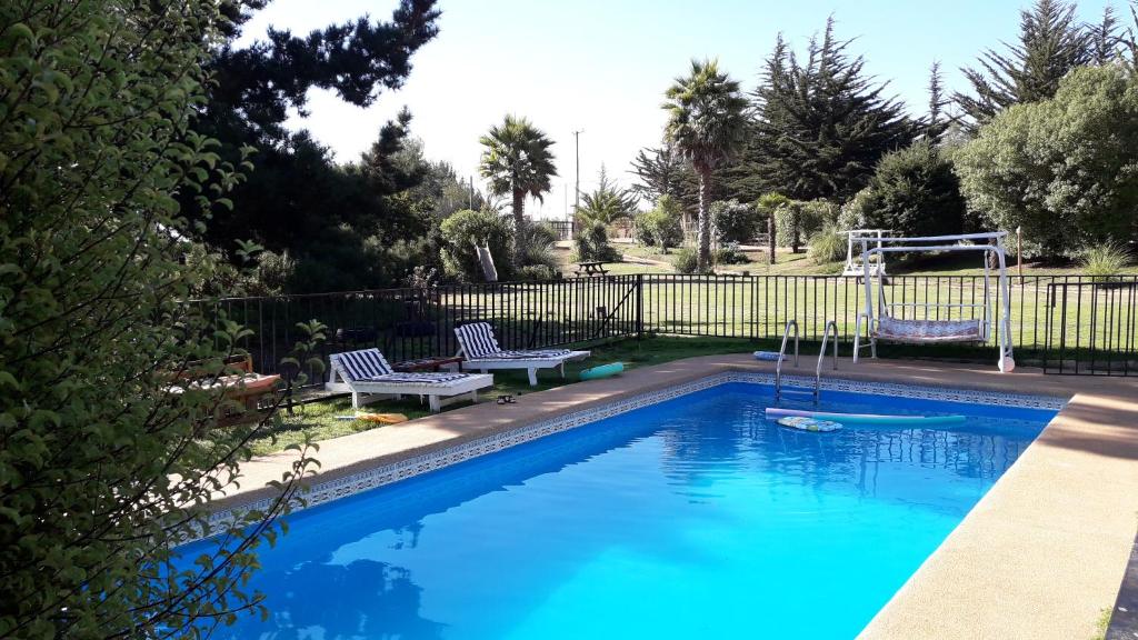 a blue swimming pool with two chairs and a fence at Algarrobo Casa Campo ALYWEN in Algarrobo