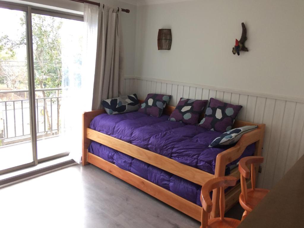 Un dormitorio con una cama con sábanas moradas y una ventana en Departamento Lacustre, en Pucón