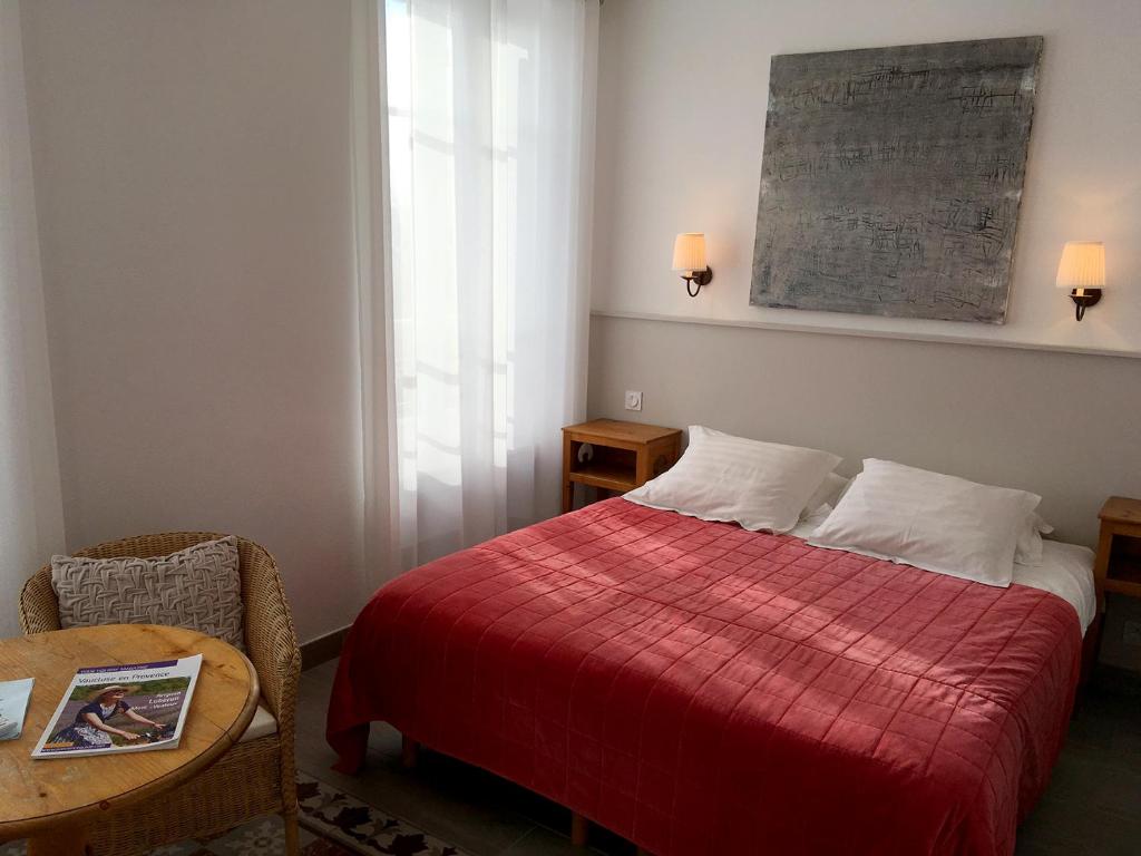 a bedroom with a bed with a red blanket and a table at La Garance in Bédoin