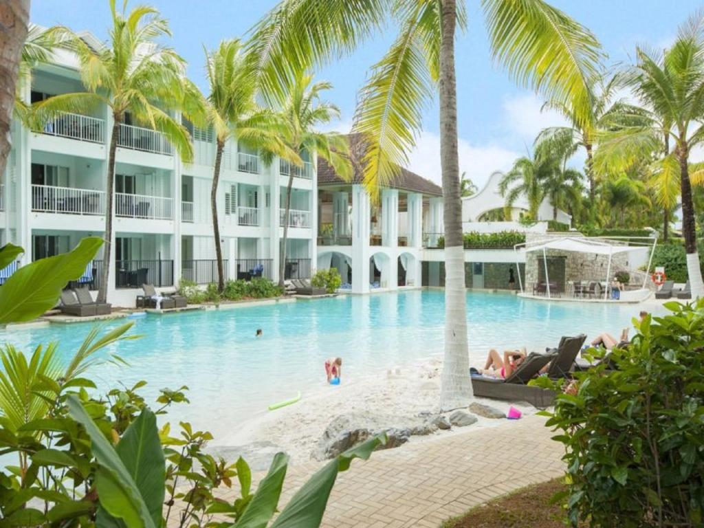 a resort pool with palm trees and people in it at Beach Club Port Douglas Luxury Apartments in Port Douglas