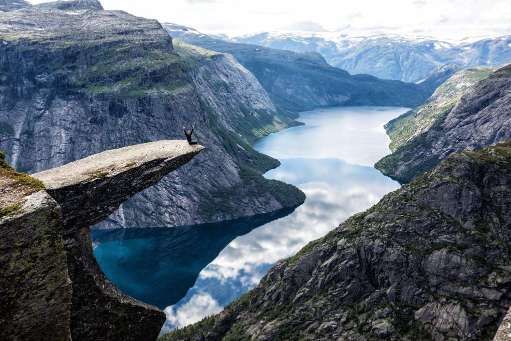 a person standing on a rock above a mountain lake at Trolltunga/Folgefonna Camp house in Jondal