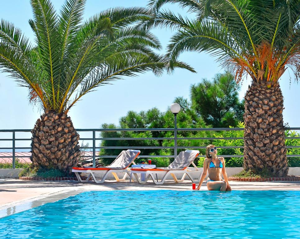 a woman sitting in a swimming pool with two palm trees at City's Hill Hotel in Kuşadası
