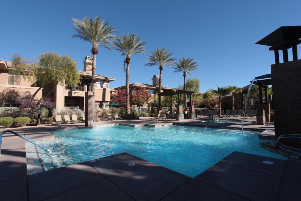 a swimming pool with palm trees in the background at The Cliffs at Peace Canyon in Las Vegas