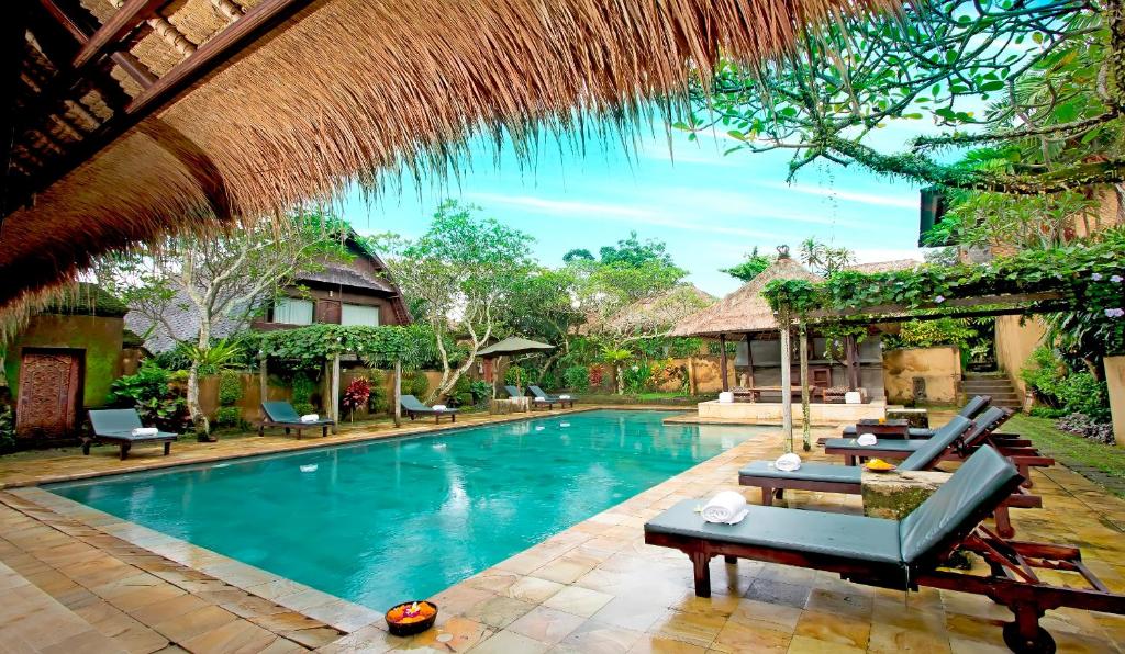 una piscina en un complejo con sillas y techo de paja en The Sungu Resort & Spa, en Ubud