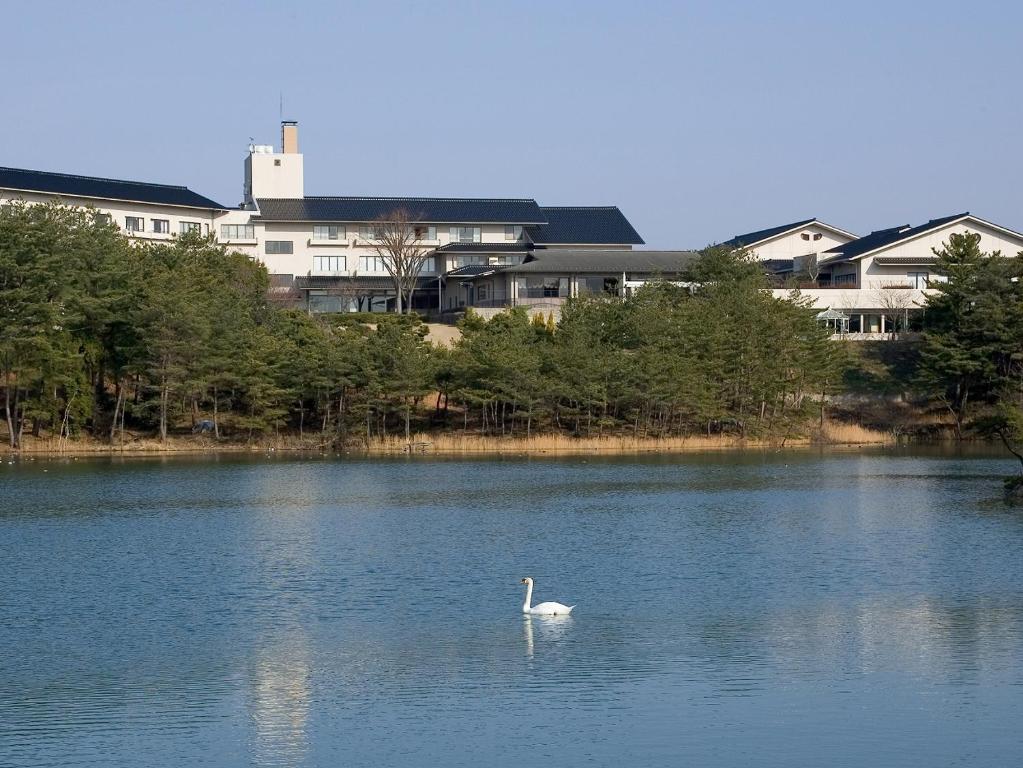 a swan swimming in a lake with buildings in the background at Ikoi no mura Notohanto in Shika