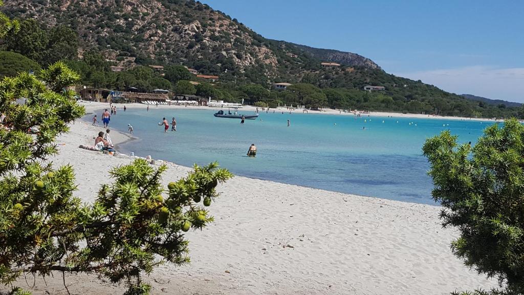 a group of people on a beach with a boat in the water at Locations Résidence Rocca Rossa Palombaggia classées 3 étoiles in Porto-Vecchio