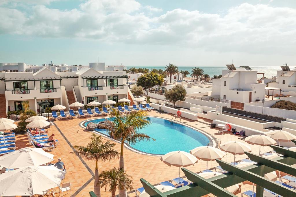 uma vista para uma piscina com guarda-sóis e para o oceano em Hotel Pocillos Playa, solo Adultos em Puerto del Carmen