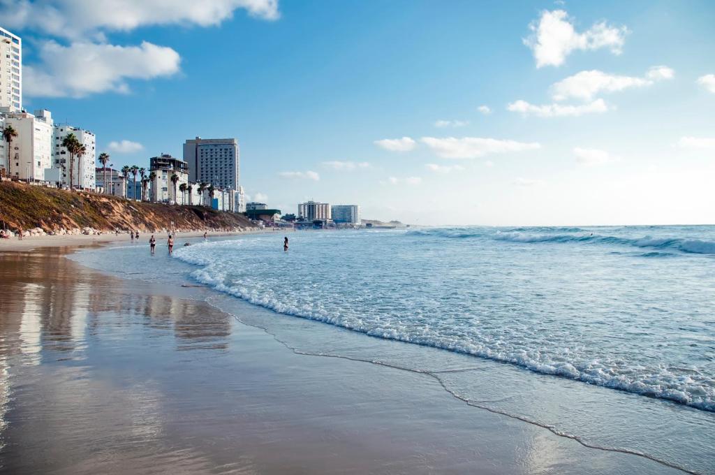 una spiaggia con persone che camminano nell'acqua e negli edifici di Arena Hotel by the Beach a Bat Yam