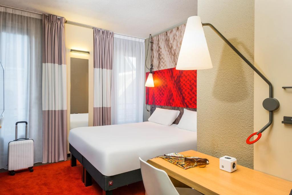 クリシーにあるキリアド パリ クリシー センターの白いベッドとデスクが備わるホテルルームです。