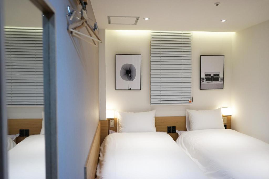 two beds in a room with white sheets and windows at Artravel Myeongdong in Seoul