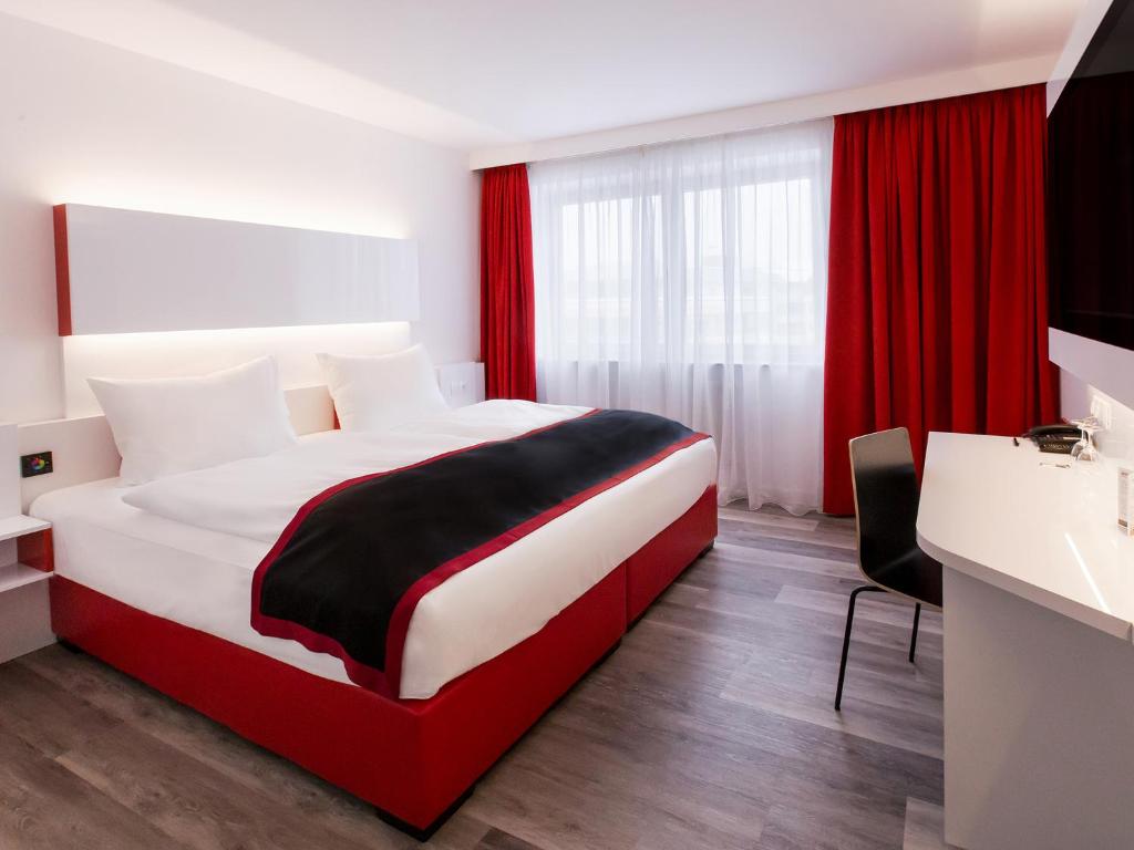 Habitación de hotel con cama roja y blanca y lavabo. en DORMERO Hotel Burghausen en Burghausen