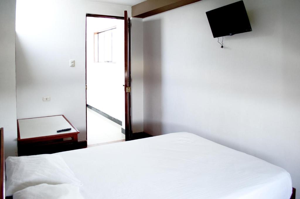 Schlafzimmer mit einem weißen Bett und einem Flachbild-TV in der Unterkunft Hostal Los Angeles in Barranca