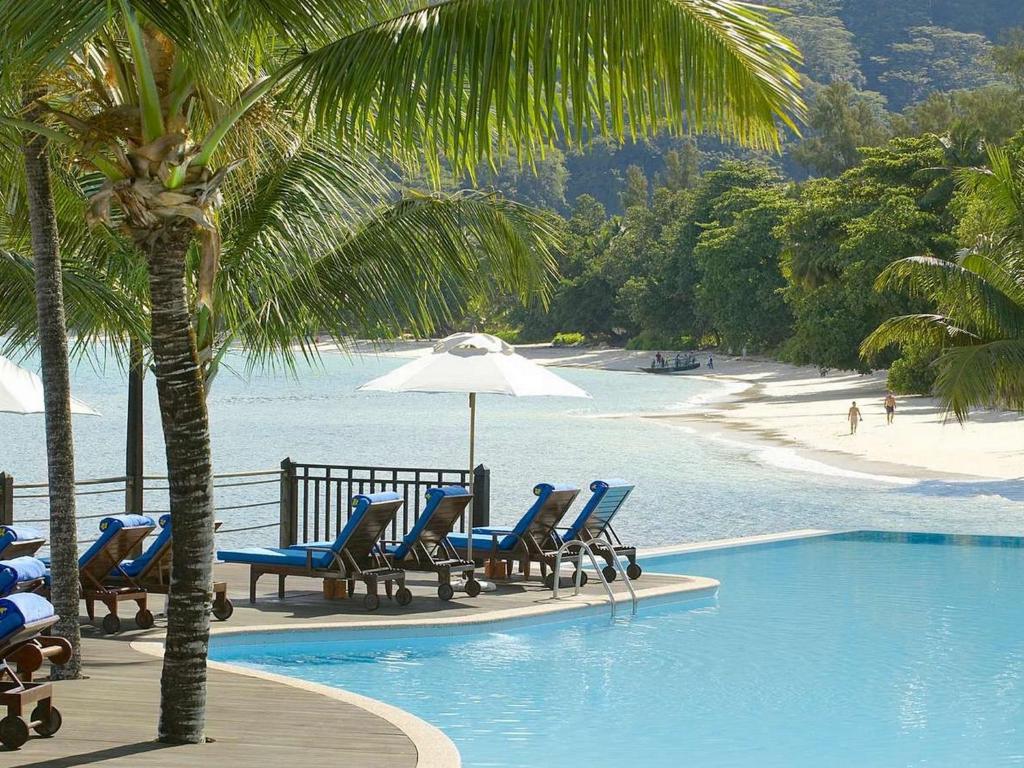a pool with chairs and an umbrella next to a beach at Fisherman's Cove Resort in Bel Ombre