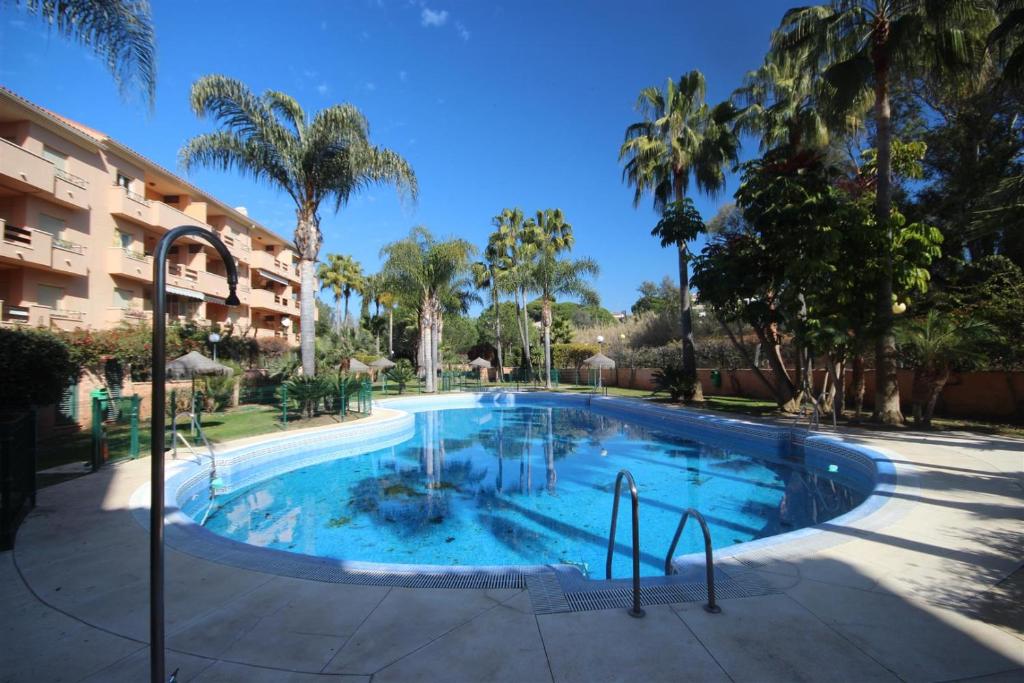 a large swimming pool with palm trees and a building at LAS DUNAS de CARIB PLAYA in Marbella