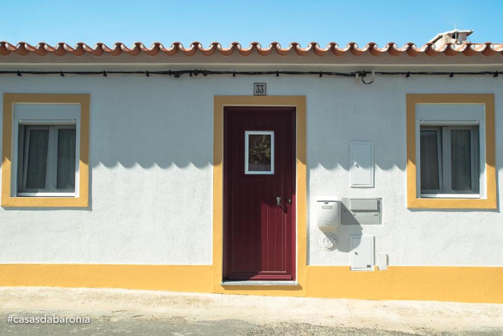 ein Haus mit einer roten Tür und zwei Fenstern in der Unterkunft Casas da Baronia in Vila Nova da Baronia