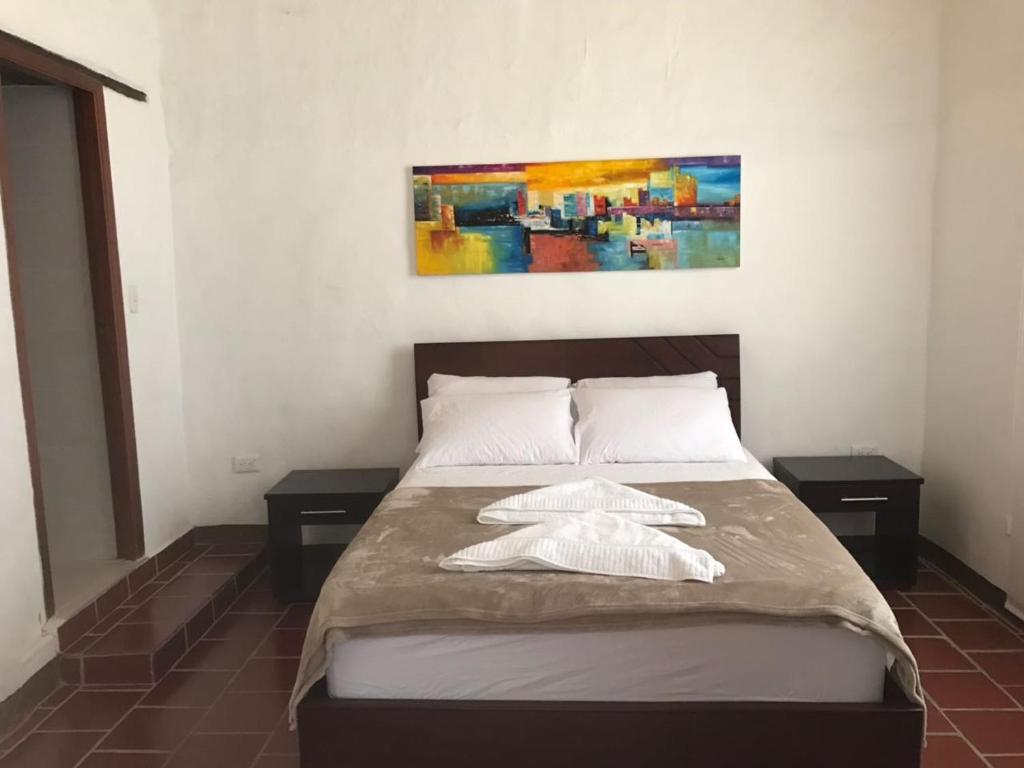 1 dormitorio con 1 cama con 2 mesas y 1 pintura en Hostal Rous San Gil, en San Gil