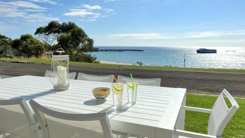 a white table with drinks on it next to the ocean at Millpond. in Penneshaw