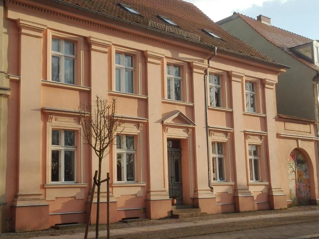 um edifício rosa com uma árvore em frente em Bed&Breakfast Wagner "im Alten Pfarrhaus" em Neuruppin