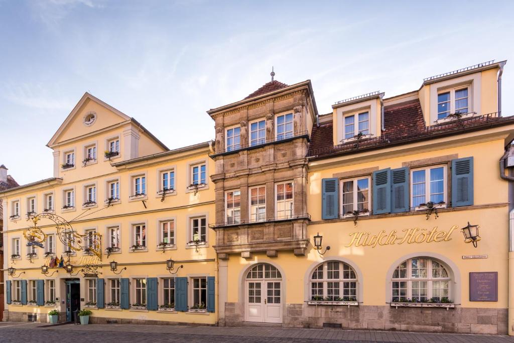 een groot geel gebouw met blauwe ramen bij Historik Hotel Goldener Hirsch Rothenburg in Rothenburg ob der Tauber