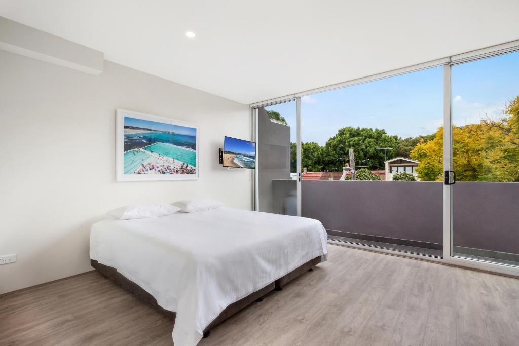 a white bedroom with a bed and a large window at Bondi Beach Studio King Suite + Balcony in Sydney