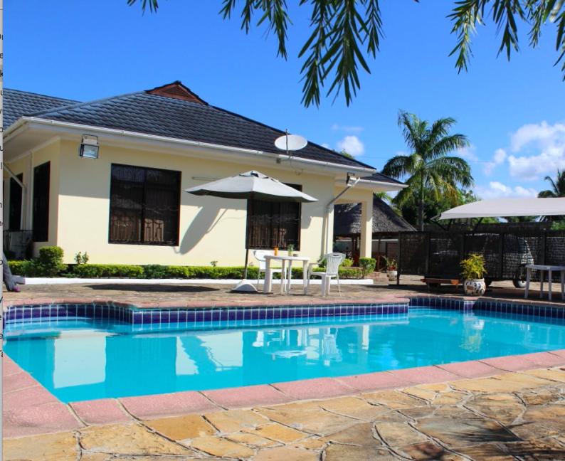 a swimming pool with an umbrella and a house at IDC Guest House in Bagamoyo